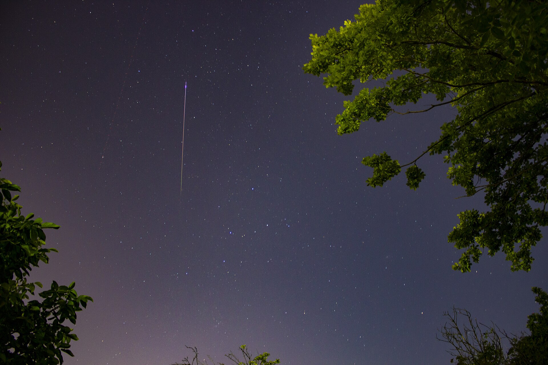 Estrella fugaz de las Perseidas cruzando un cielo nocturno estrellado sobre un paisaje oscuro